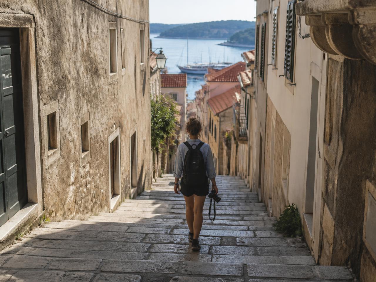 A solo traveller with a camera walking a stone street down to the harbour